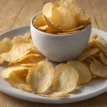 Close-up of crispy golden Yukon Gold potato chips on a rustic wooden table under natural light.