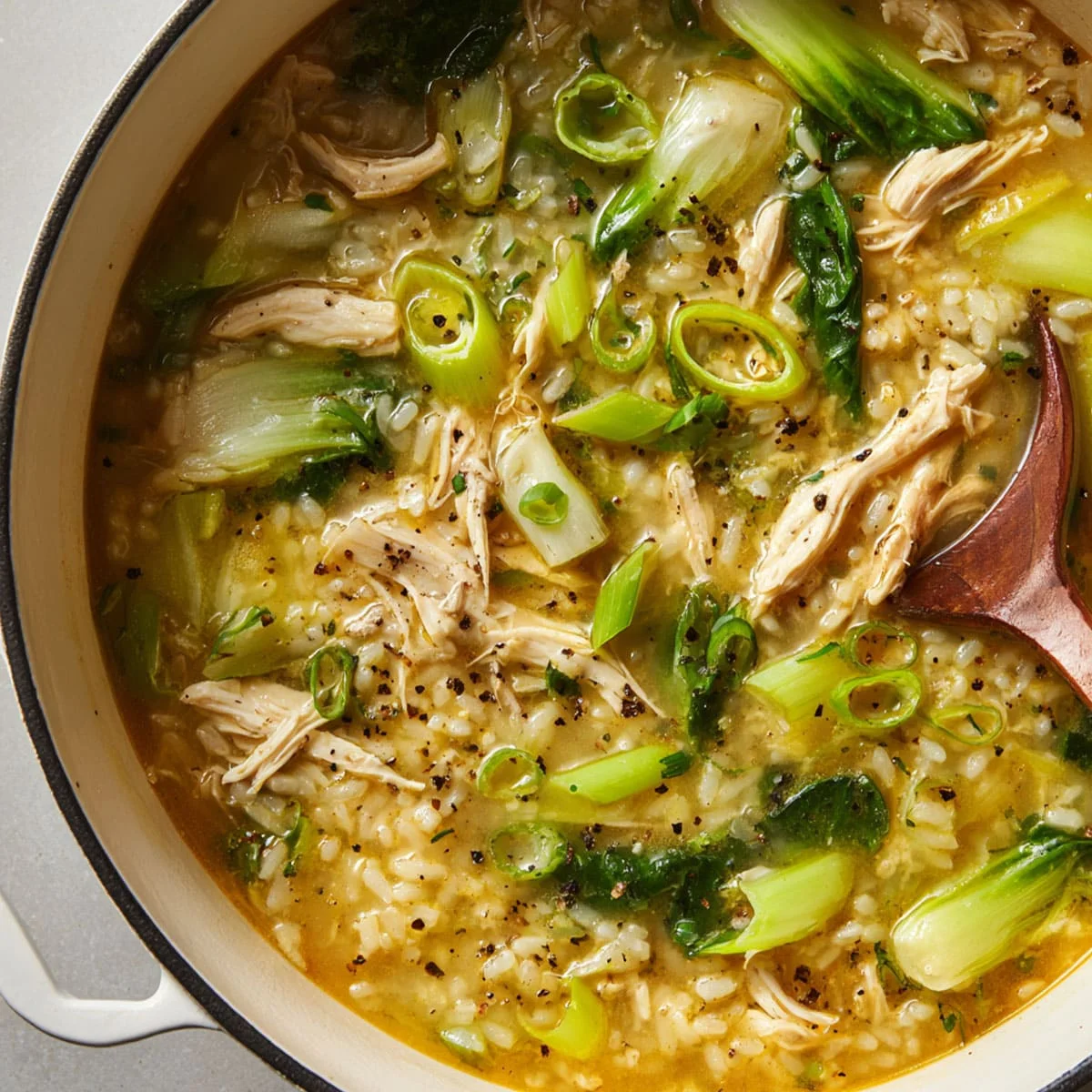 Spoonful of ginger chicken and rice soup showing tender chicken, rice, and bok choy.