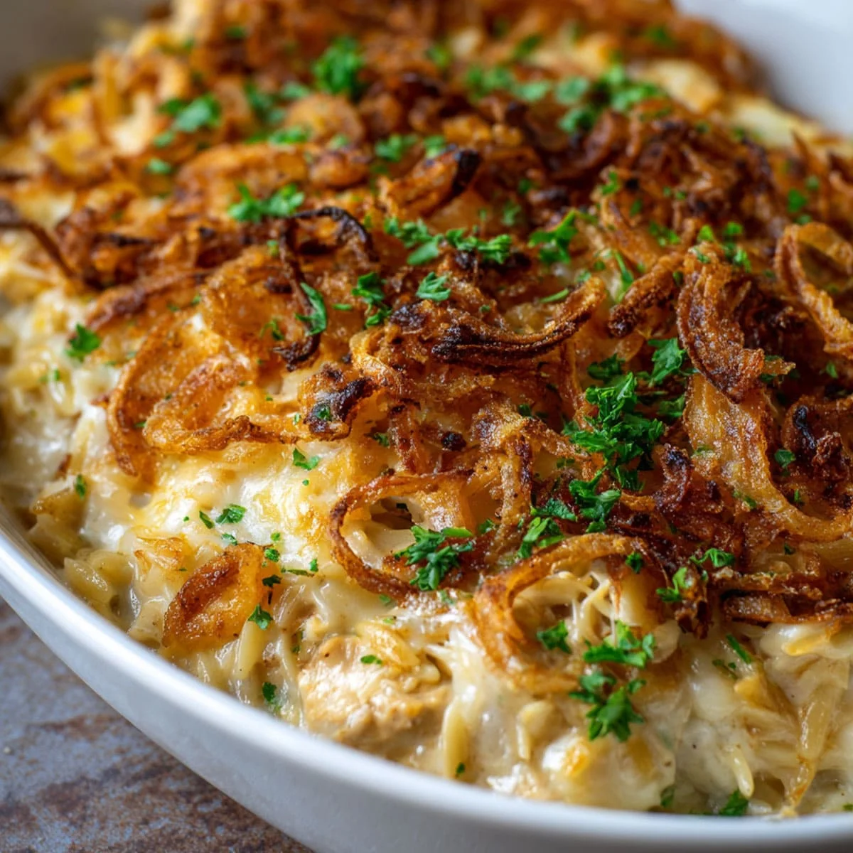 French Onion Chicken Orzo Casserole topped with crispy caramelized onions and melted cheese in a white baking dish