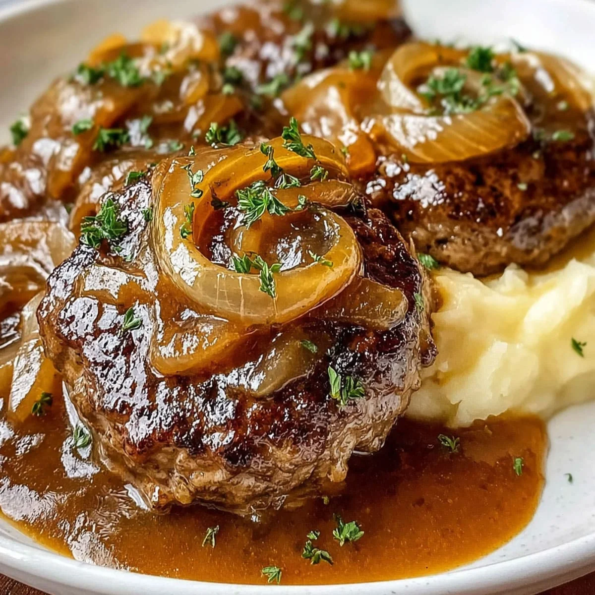 Juicy hamburger steak and gravy with caramelized onions served over mashed potatoes and garnished with parsley.