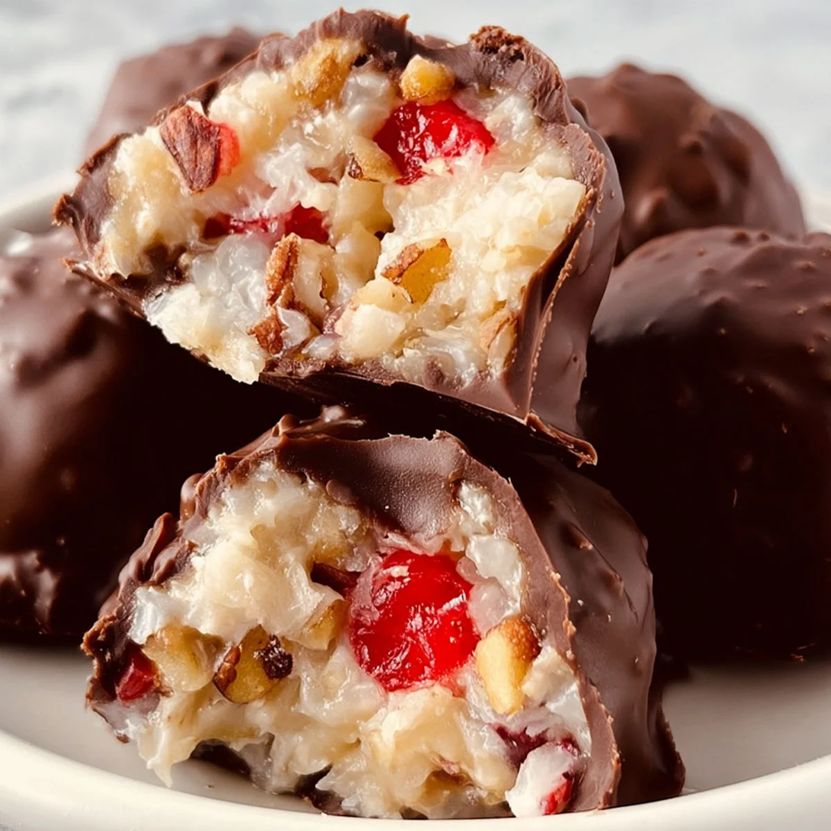 Close-up of sliced Martha Washington Candy showing the chewy coconut center with red cherries and chopped pecans inside a dark chocolate shell.