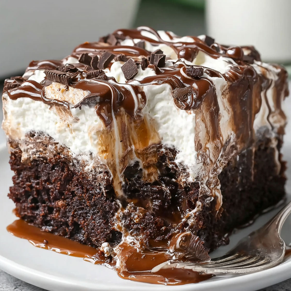 Chocolate Poke Cake with Marshmallow topping dripping with rich chocolate ganache and whipped cream on a dessert plate.