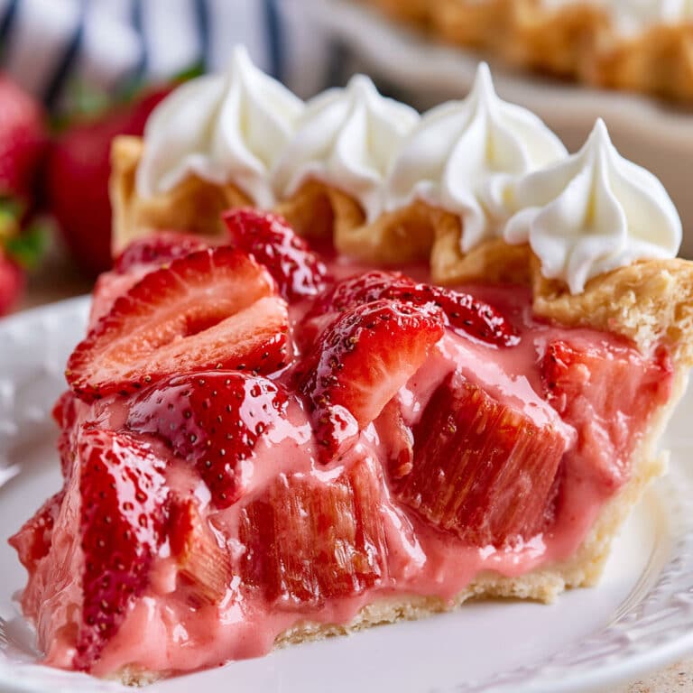 Creamy Strawberry Rhubarb Pie slice with flaky crust, glossy strawberries, rhubarb chunks, and whipped cream topping
