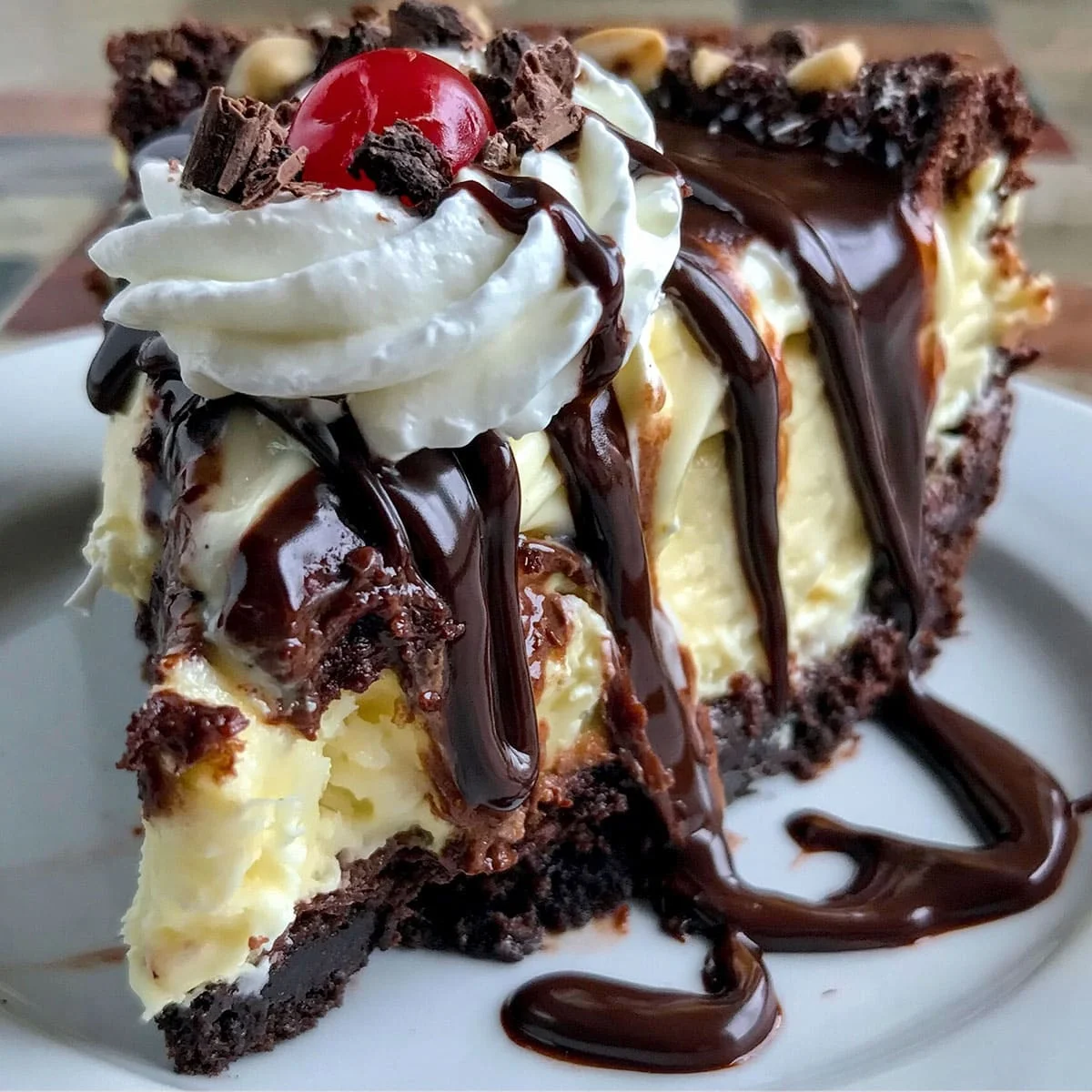 hot fudge sundae brownie cheesecake recipe slice with melted chocolate drizzle and creamy cheesecake filling