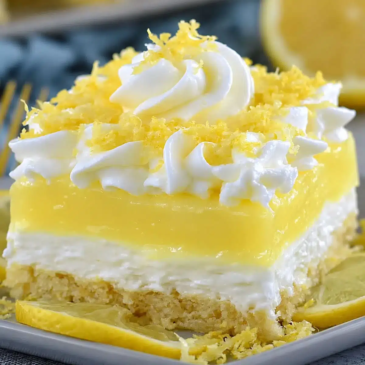 No Bake Lemon Cream Dessert Bars Recipe slice with buttery crust, fluffy cream cheese layer, glossy lemon pudding, whipped cream, and lemon zest.