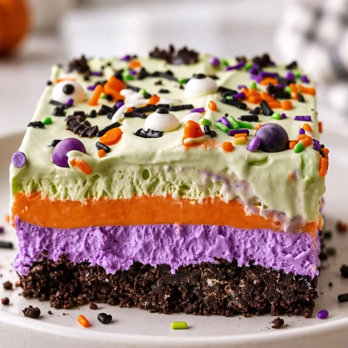 Halloween Lush with a chocolate cookie crust, purple cheesecake, orange pudding, green topping, and festive sprinkles